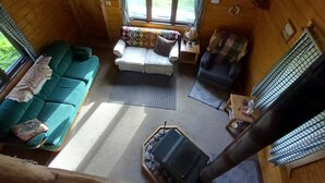Ein gemütliches Blockhauss-Interieur mit einer Couch, einem kleinen Tisch und einem Fenster mit Blick auf Grünflächen.