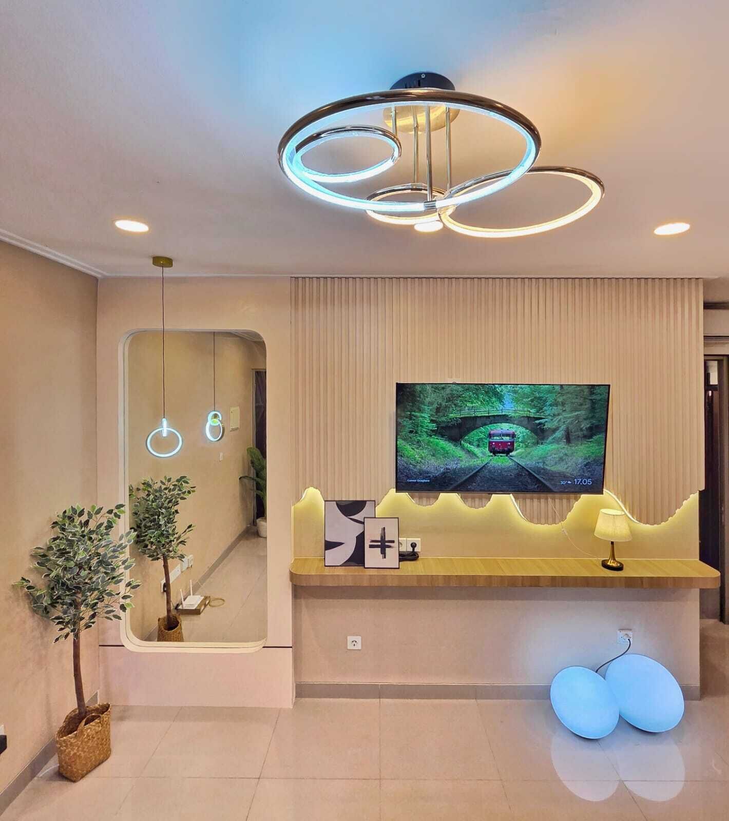 A modern reception area with a large flat-screen TV mounted on a wall, a reception desk with a mirror, and a unique circular light fixture above.