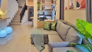 A modern living room with a sofa, a coffee table, and a staircase leading to a kitchen. - LeGacy By SanLiving - 3BR - PIK2 (Kosambi)