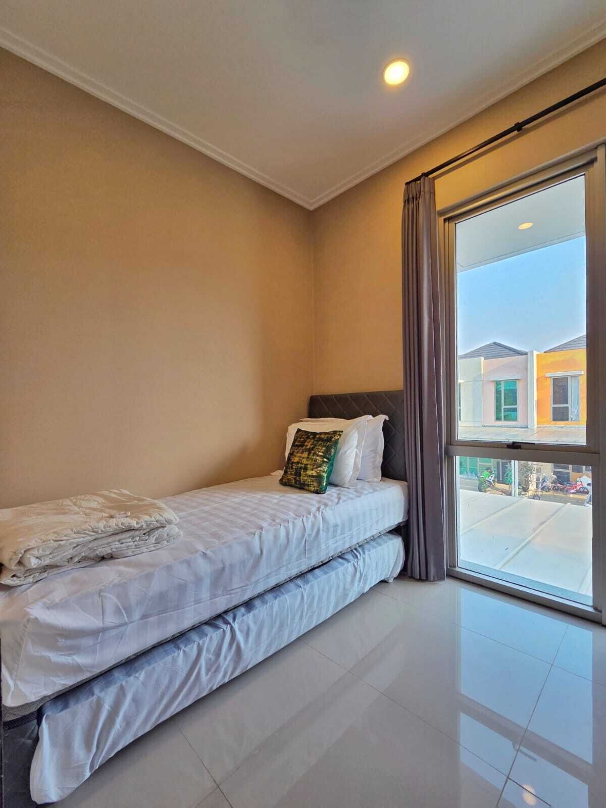 Una habitación pequeña con una cama individual, un ventanal grande y vistas a edificios.