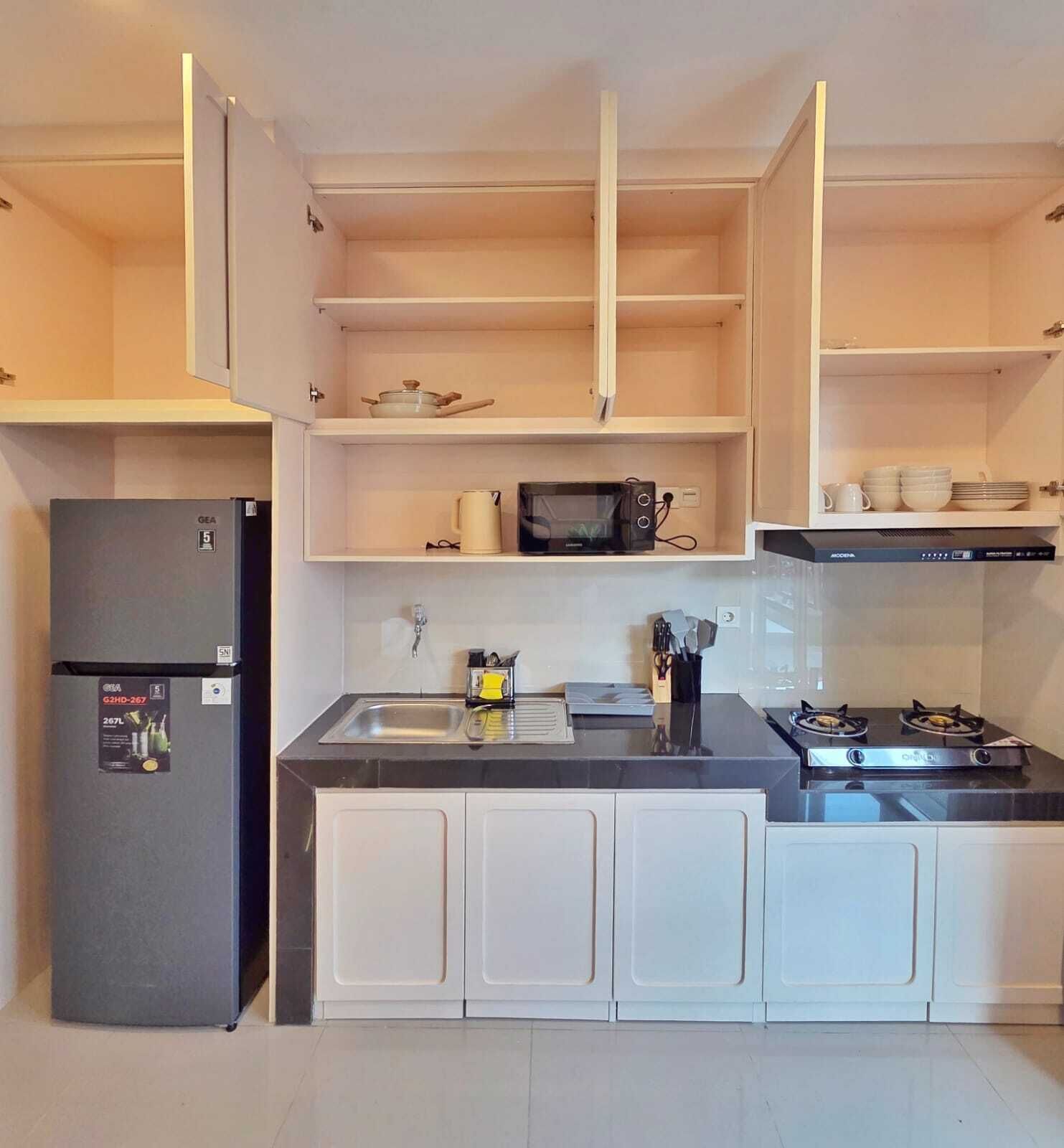 Eine kompakte Küche mit weißen Schränken, einer schwarzen Arbeitsplatte, einer eingebauten Mikrowelle, einem Gasherd und einem Kühlschrank.