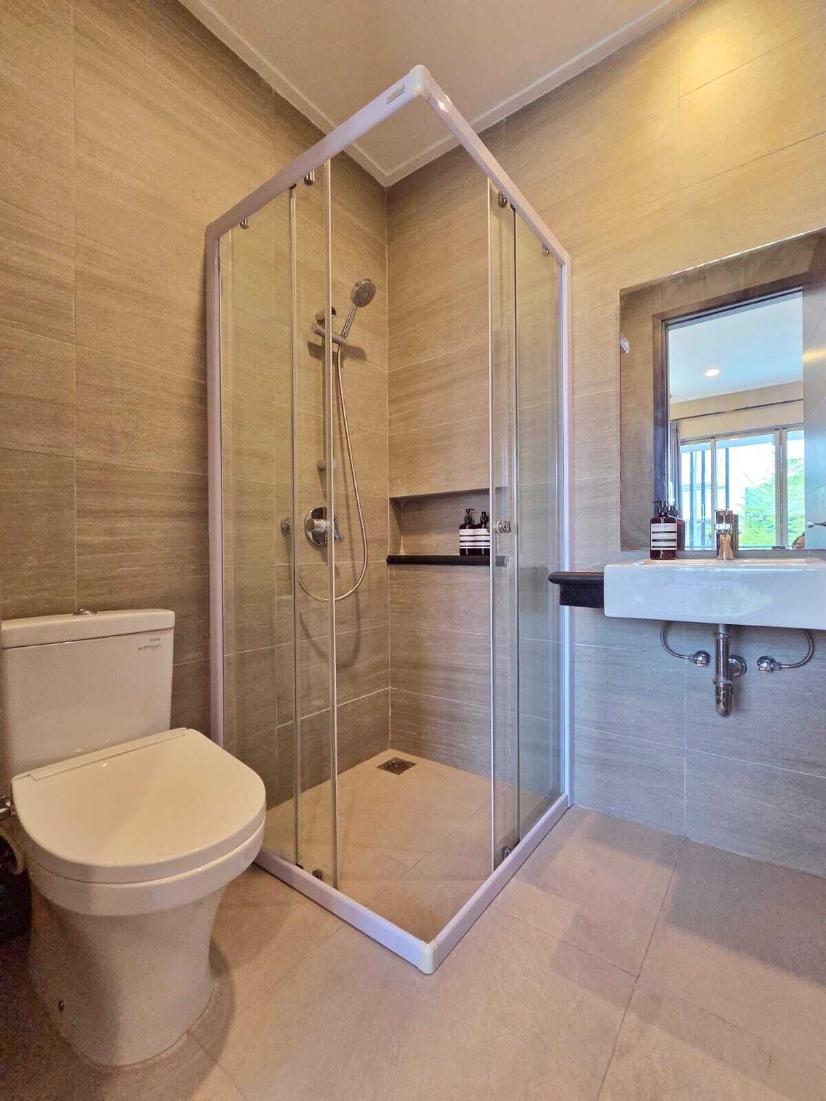 Un baño moderno con ducha envuelta en vidrio, un inodoro y un lavamanos con ventana superior.