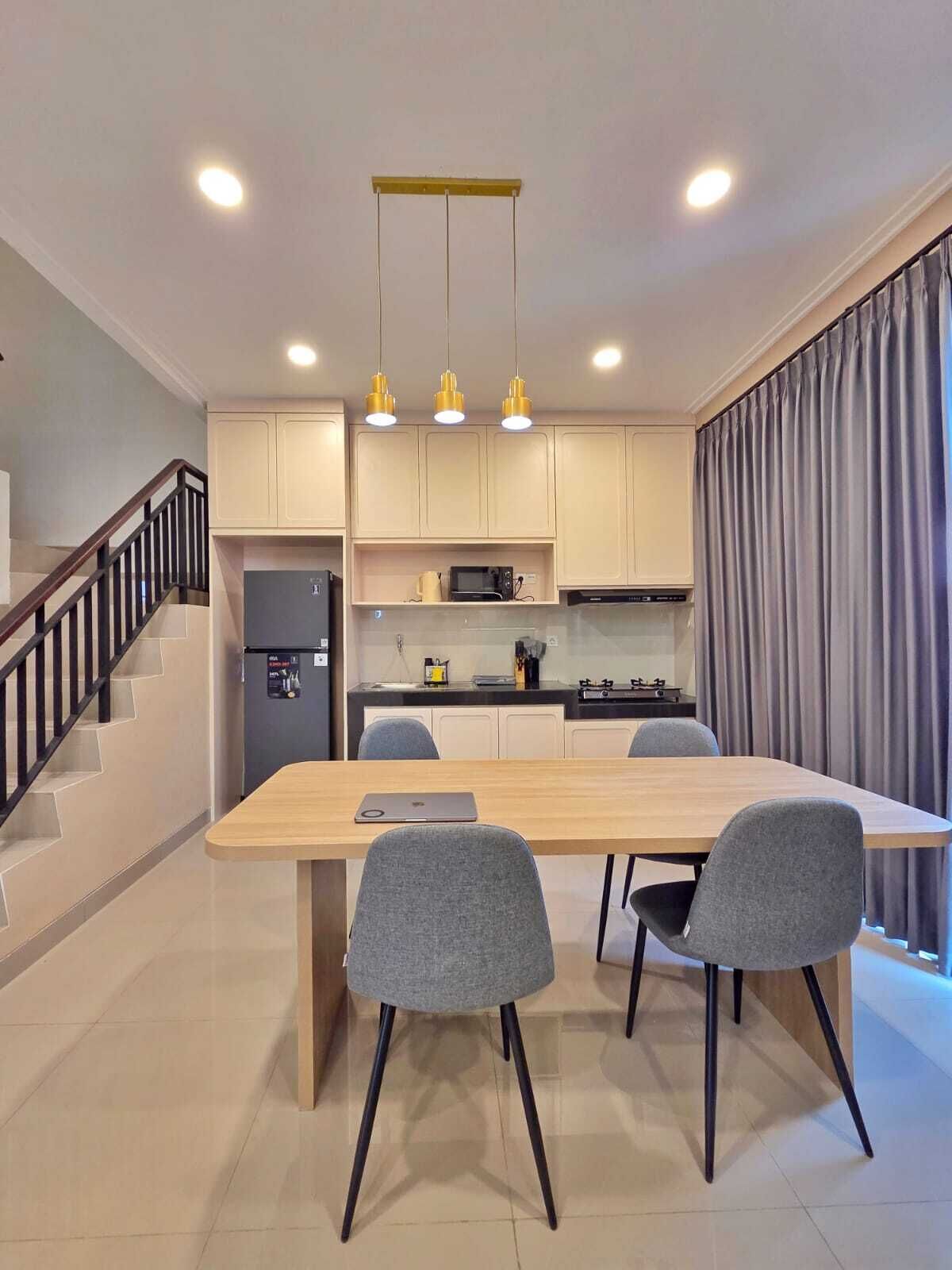 A modern kitchen with a central island, a dining table with chairs, and a staircase with a railing.