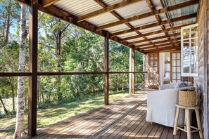 Eine Holzterrasse mit überdachtem Bereich, einem weißen Sofa und einem Korbstuhl.