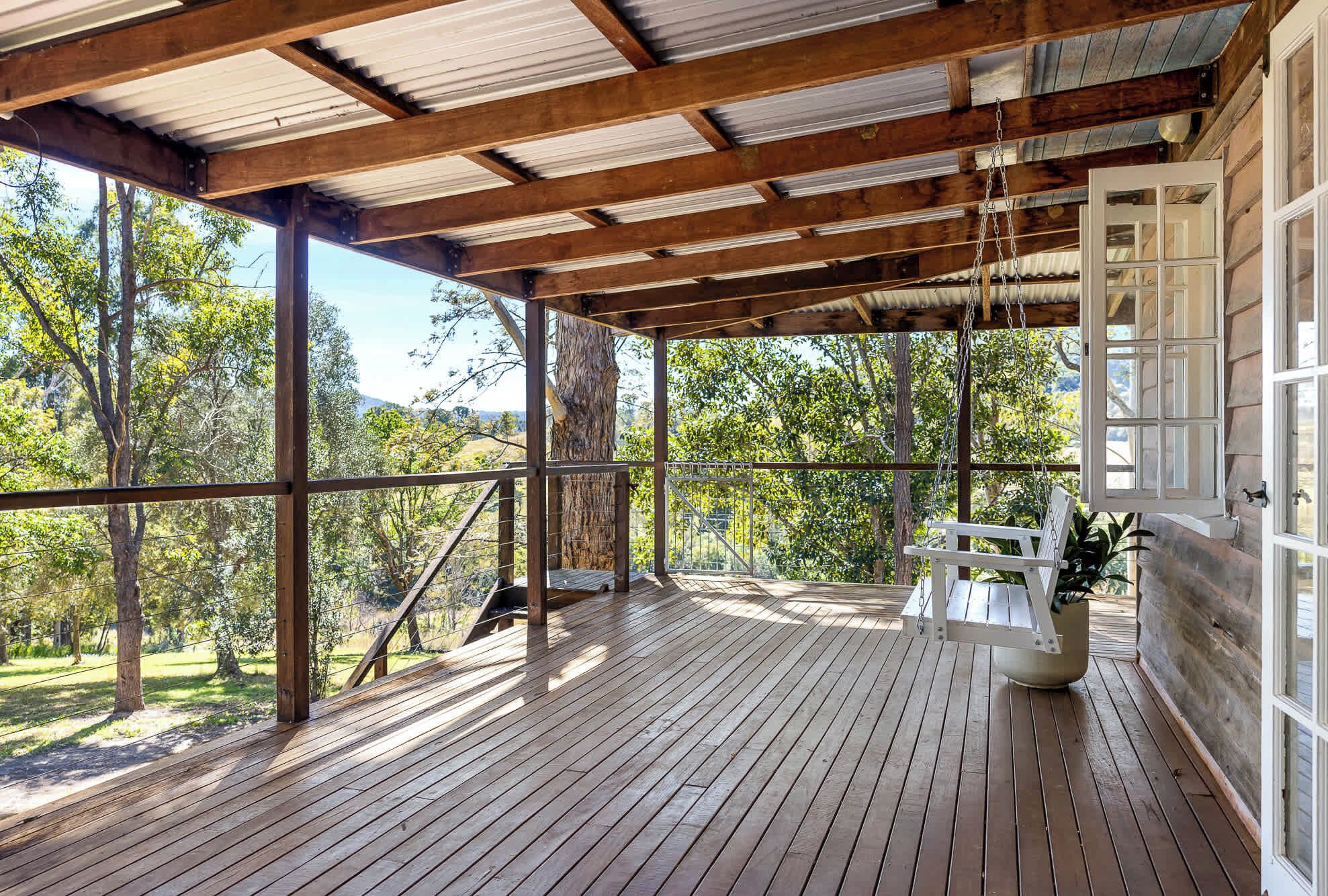 A covered wooden deck with a swing chair, large windows, and a view of the surrounding trees.