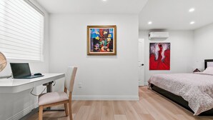 Un dormitorio moderno con escritorio, computadora portátil, silla, cama y dos cuadros.