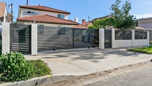 Una zona residencial privada con cerramiento moderno, un camino de entrada de hormigón y una casa con tejado de tejas.