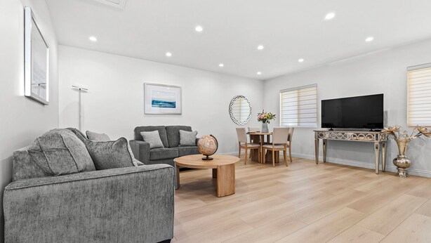 Una sala de estar moderna con un sofá gris, una mesa de centro, un mueble para televisión y un comedor con sillas y una mesa.
