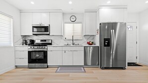 Una cocina moderna con armarios blancos, un refrigerador de acero inoxidable, un microondas, un horno y un fregadero.