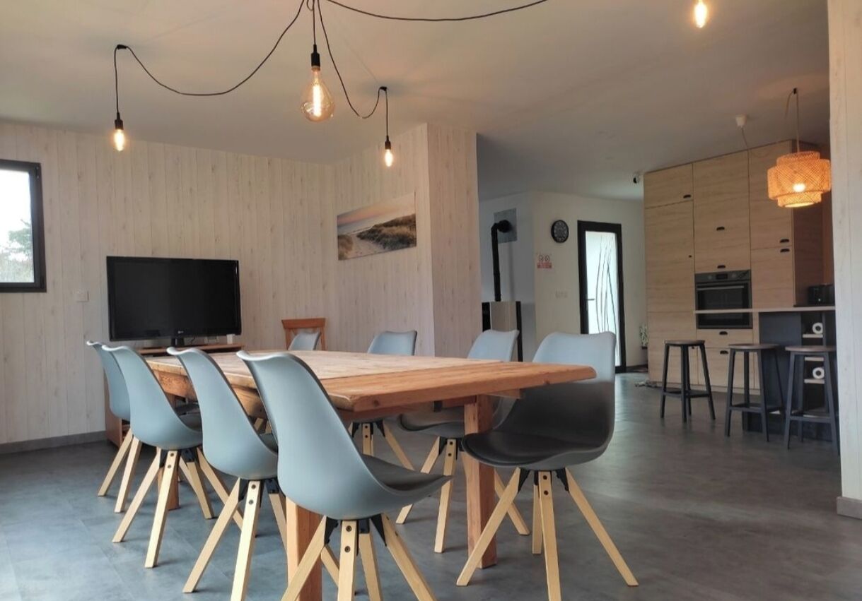 Een moderne eetruimte met een houten tafel en stoelen, een flatscreen televisie en hanglampen.