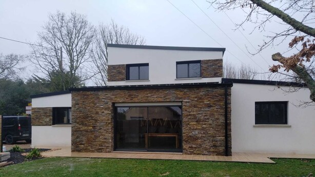 Ein modernes, zweistöckiges Haus mit Natursteinfassade, großen Schiebeglastüren und einer Flachdachkonstruktion.