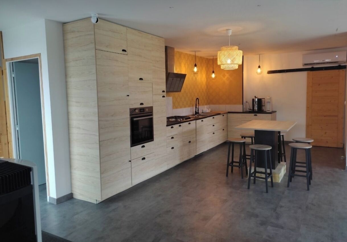 Une cuisine moderne avec des meubles en bois, un îlot central doté de tabourets, un éclairage suspendu et un four.