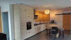 Eine moderne Küche mit Holzausstattung, einer zentralen Kochinsel mit Hockern, Pendelleuchten und einem Backofen.