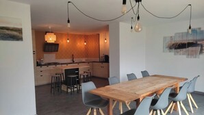 Eine moderne Küche mit einem Holztisch und Stühlen, einer Hängeleuchte und Blick in den Essbereich.
