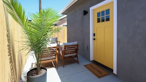 Une petite terrasse avec une chaise en bois, une plante en pot et une porte jaune.