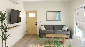 Un salon comprenant un canapé, une table basse, un téléviseur fixé au mur, une porte et un lave-linge.