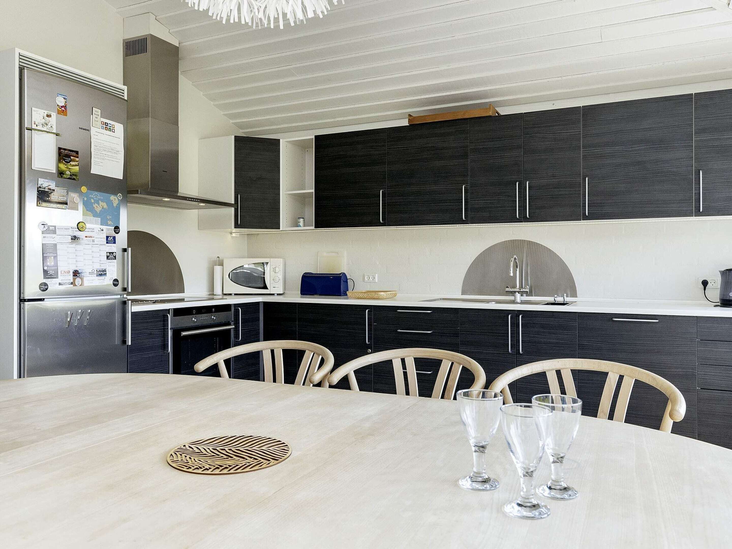Une cuisine moderne avec des meubles de couleur sombre, un plan de travail blanc et une table à manger avec des chaises.