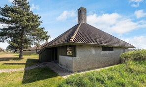 Een laag, eenlaags gebouw met een pannendak en schoorsteen, omringd door gras en bomen.