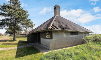 A small, single-story building with a tiled roof and a chimney, surrounded by grass and trees.