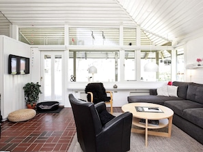 A modern living room with a sofa, a round coffee table, a black chair, a television mounted on the wall, and a large window with decorative items.