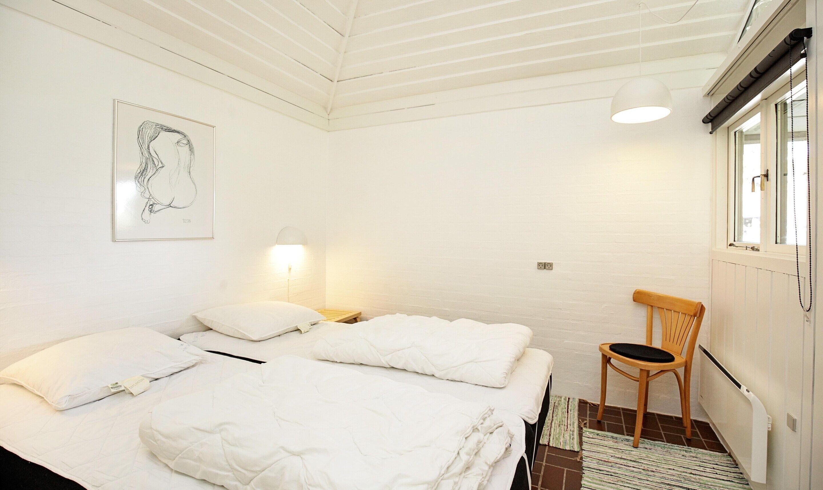 A room with two beds, a wooden chair, a wall-mounted lamp, and a radiator.