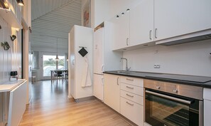 A modern kitchen with white cabinets, a stainless steel oven, and a dining area with a table and chairs. - Karrebaeksminde Fjordhouses (Karrebæksminde)