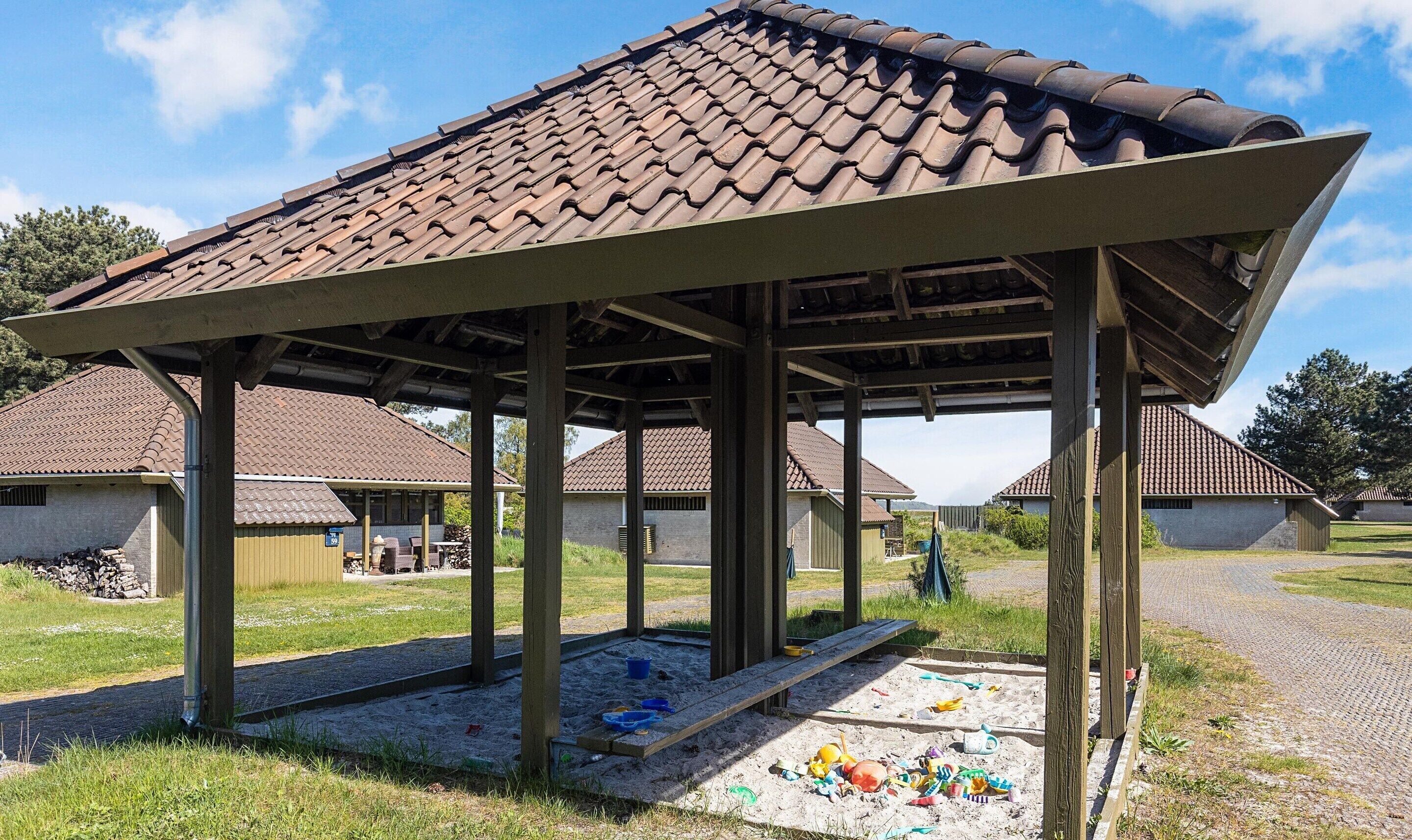 A covered outdoor area with a tiled roof, wooden beams, and a sandy play area with toys.
