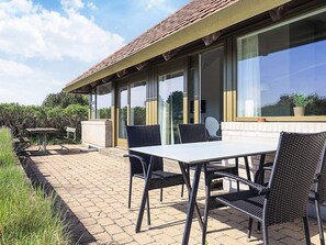 Een terras buiten met een tafel en stoelen, een pad van bakstenen en een gebouw met grote ramen.