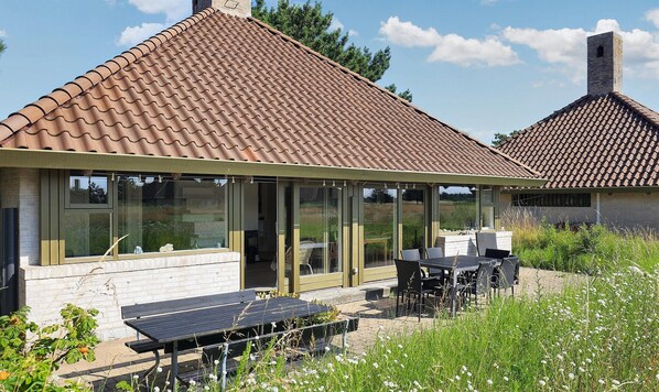 Een modern huis met pannendak, grote glasramen en een terras met een tafel en stoelen.