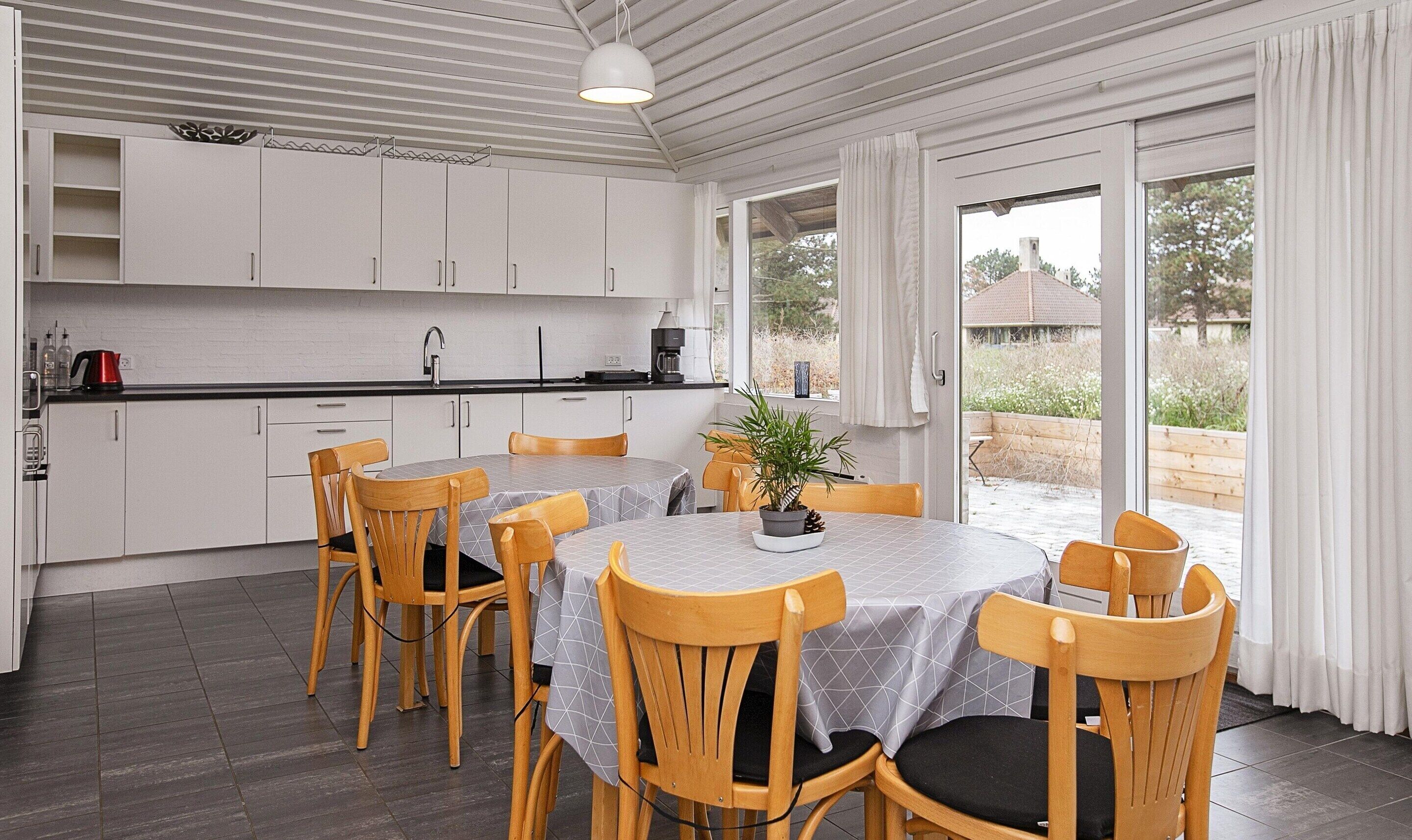 Une cuisine moderne avec des meubles blancs, un plan de travail noir et un coin repas comprenant des chaises et une table en bois.