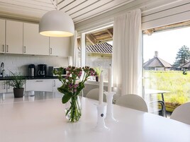 Una cocina moderna con armarios blancos, una mesa de comedor con un jarrón de flores y vistas a un paisaje rural.