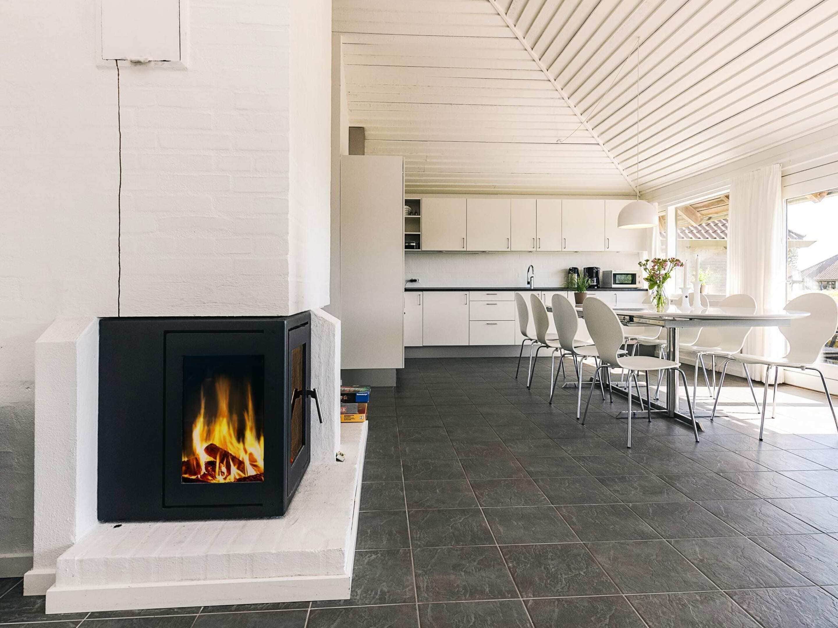 A modern kitchen with white cabinets, a fireplace, and a dining area with chairs and a table.