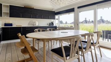 A modern kitchen with dark cabinets, a white countertop, and a large window overlooking a green landscape.
