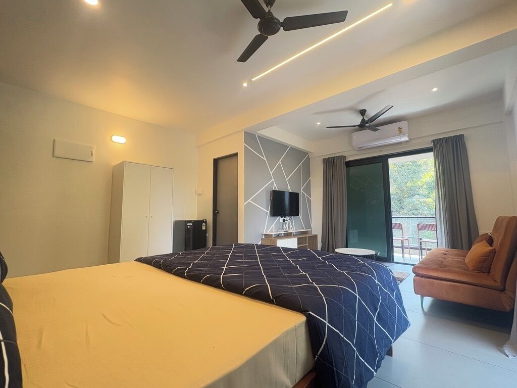 A modern hotel room with a bed, a sofa, a TV, and a ceiling fan.