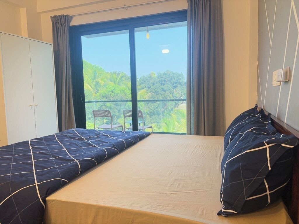 Une chambre avec deux lits, un balcon avec une chaise et une vue sur la verdure.