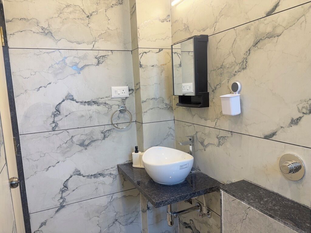 A bathroom with a marble wall, a white sink, a mirror, and a towel dispenser.