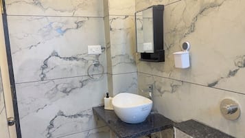 A bathroom with a marble wall, a white sink, a mirror, and a towel dispenser.