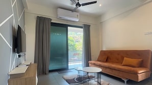 A modern living room with a sofa, a TV, a ceiling fan, and a sliding glass door leading to a balcony. - CasaMandrem (Mandrem)