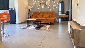A modern living room with a sofa, a small round table, and a chair. There is a lamp, a clock, and artwork on the wall. - CasaMandrem (Mandrem)