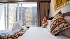 A hotel room with a large bed, a view of a stone wall and a balcony. - Lumbung Sari Studio (Kuta)