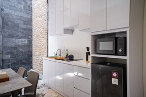 A compact kitchen with white cabinets, a built-in microwave, and a refrigerator. - Lumbung Sari Studio (Kuta)