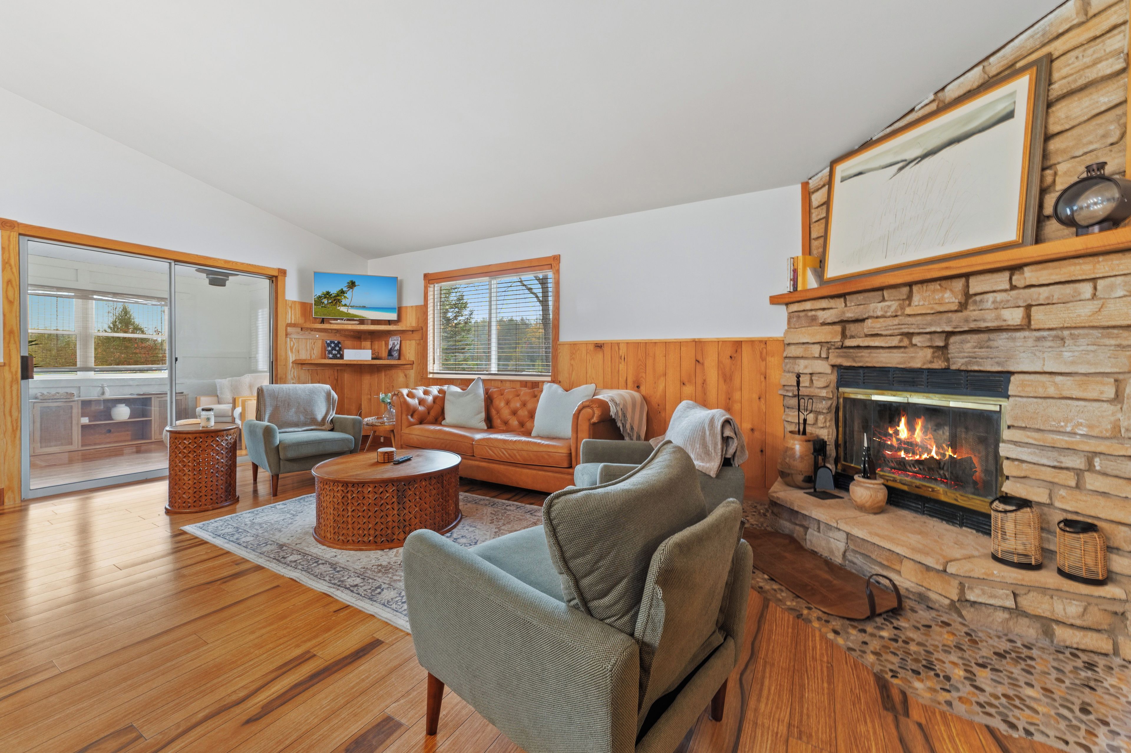 A spacious living room with a fireplace, wooden flooring, and a large window with blinds.