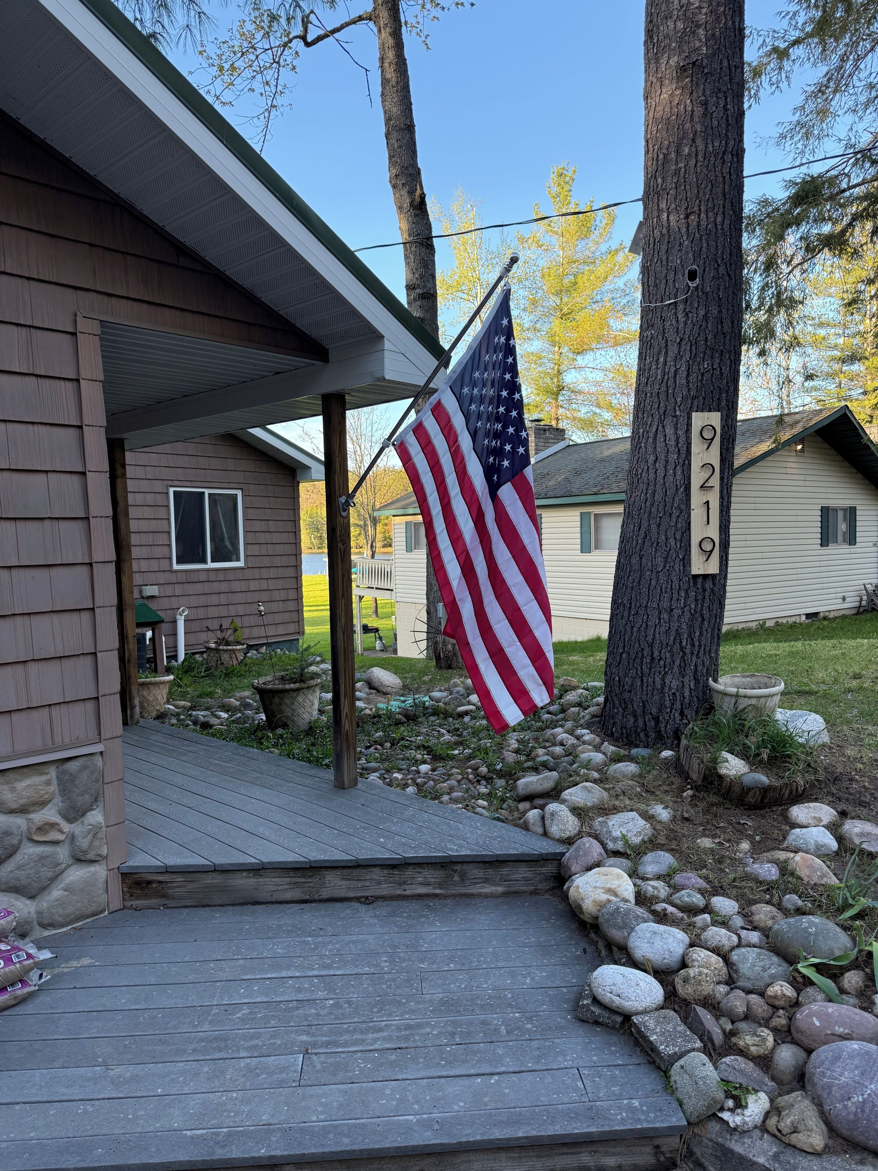 A house with a porch, an American flag, a mailbox, and a number 9219 sign on a tree.