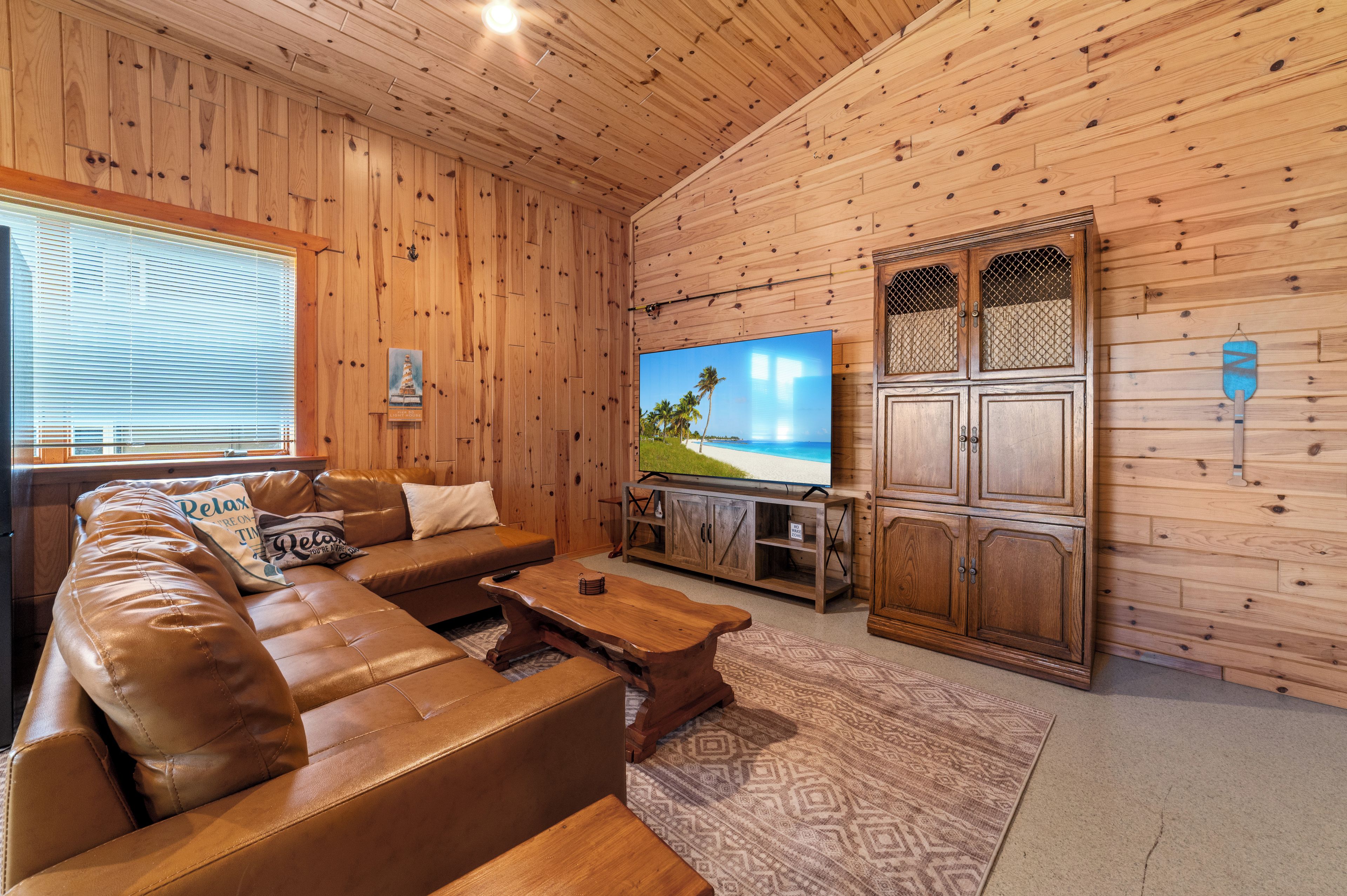 A wooden-paneled room with a leather sofa, a flat-screen TV, and a cabinet.
