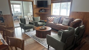 Un salon comprenant un canapé, des fauteuils, une table basse, un téléviseur et une grande fenêtre.