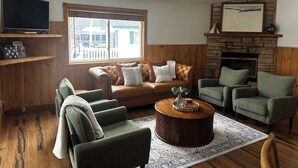 Un salon avec un canapé en cuir marron, des fauteuils verts, une table basse ronde en bois et une cheminée en pierre.