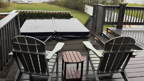 Une terrasse en bois avec deux fauteuils Adirondack et une petite table, donnant sur une étendue d’eau.