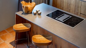 Eine moderne Küche mit einer zentralen Kochinsel, zwei Holzbarhocker und einer besonderen Holbschüssel auf der Arbeitsplatte.