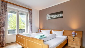 A bedroom with a wooden bed, white bedding, a nightstand with a lamp, and a window with curtains. - Group house in Fügen , Zilltertal Arena (Fügen im Zillertal)