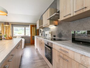 Eine moderne Küche mit Holzschränken, einer großen Kochinsel, Edelstahlgeräten und Blick auf Grünfläche.